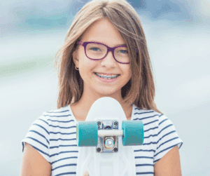 Smiling girl with braces and glasses holding a skateboard outdoors