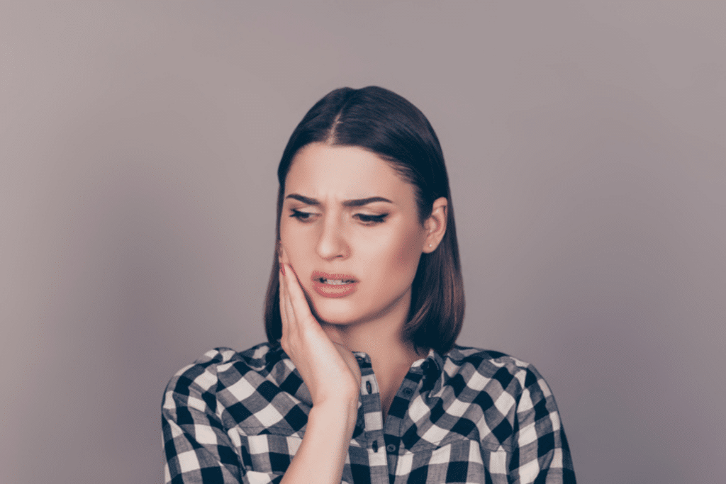 Young woman holding her cheek while experiencing jaw or tooth pain