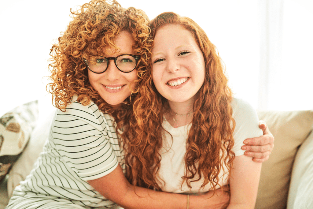 Smiling mother with glasses embracing her young daughter, both with curly hair
